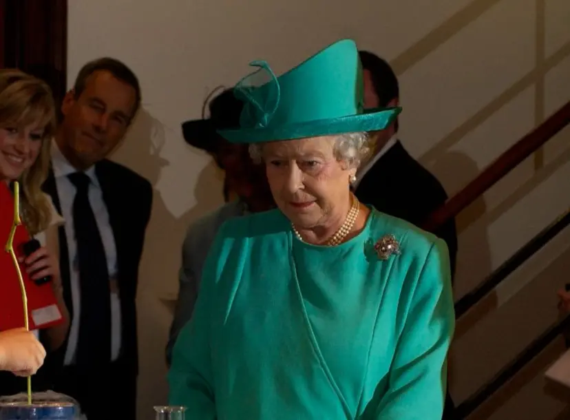 Her Majesty the Queen wearing a green dress and hat, watching a science demonstration