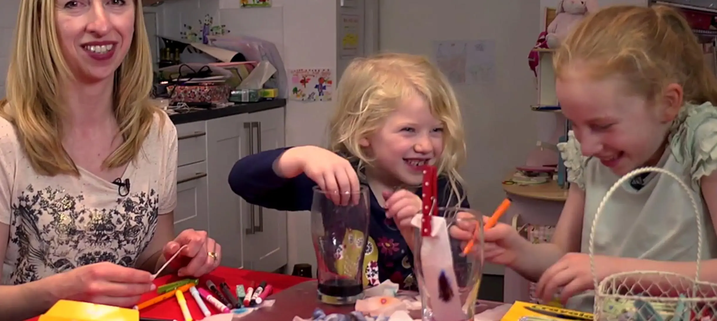 a woman and two toung girls laughing and doing a science experiment with felt tip pens, kitchen paper and water