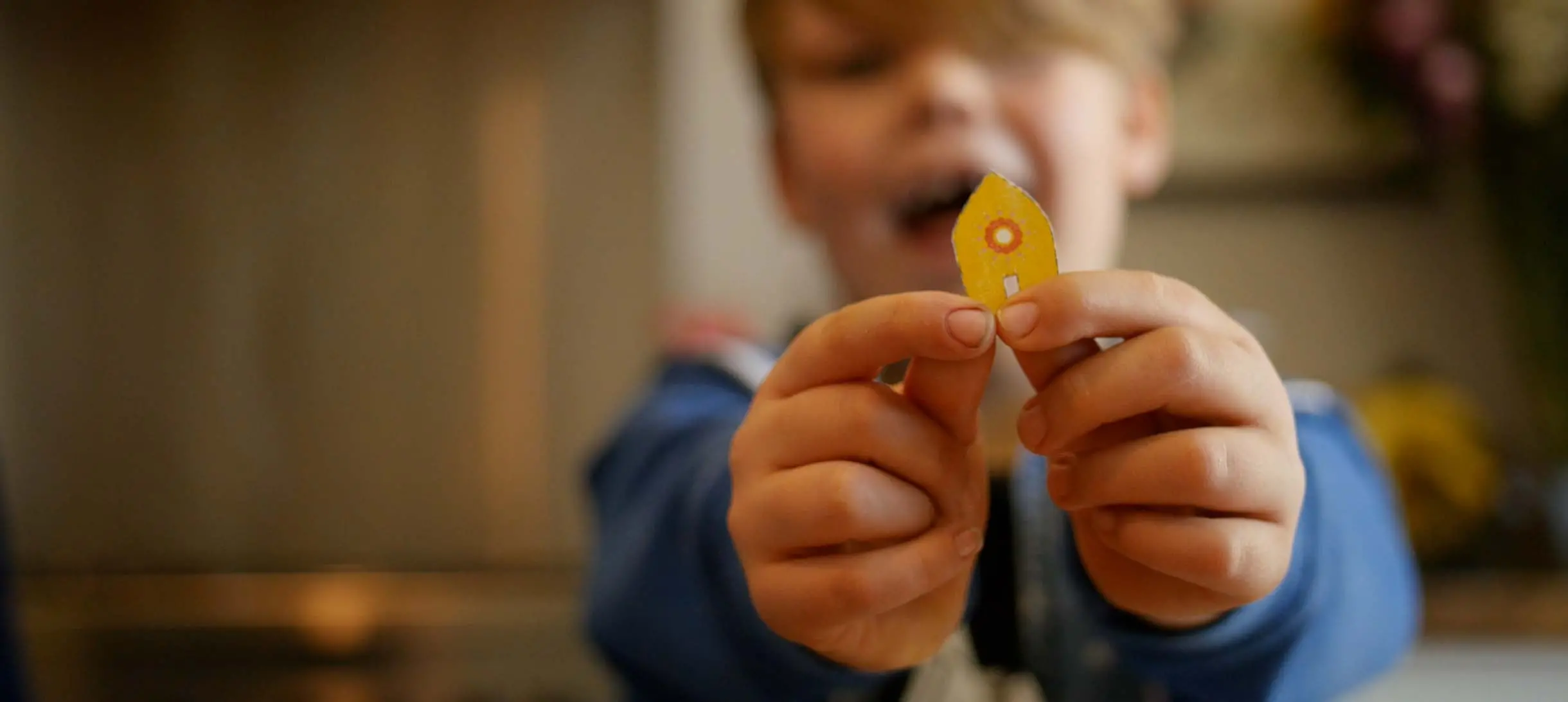 a small boy holds a small piece of cardboard shaped like a boat