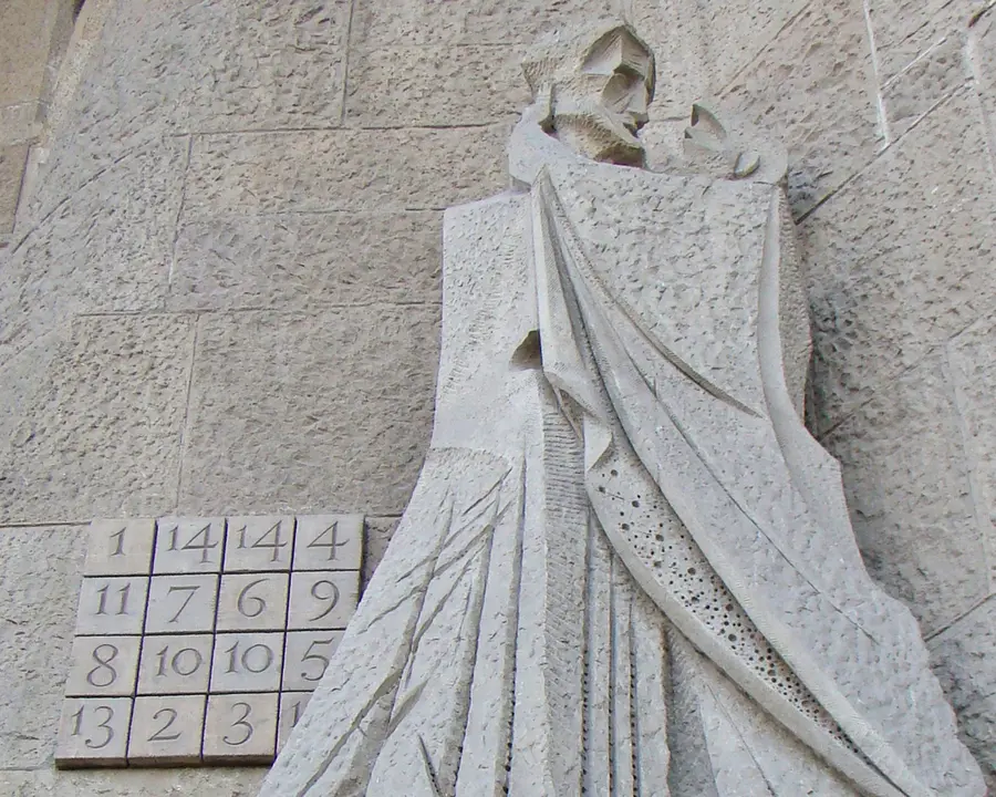 A stone magic square on the side of the Sagrada Familia, next to a statue of two people kissing