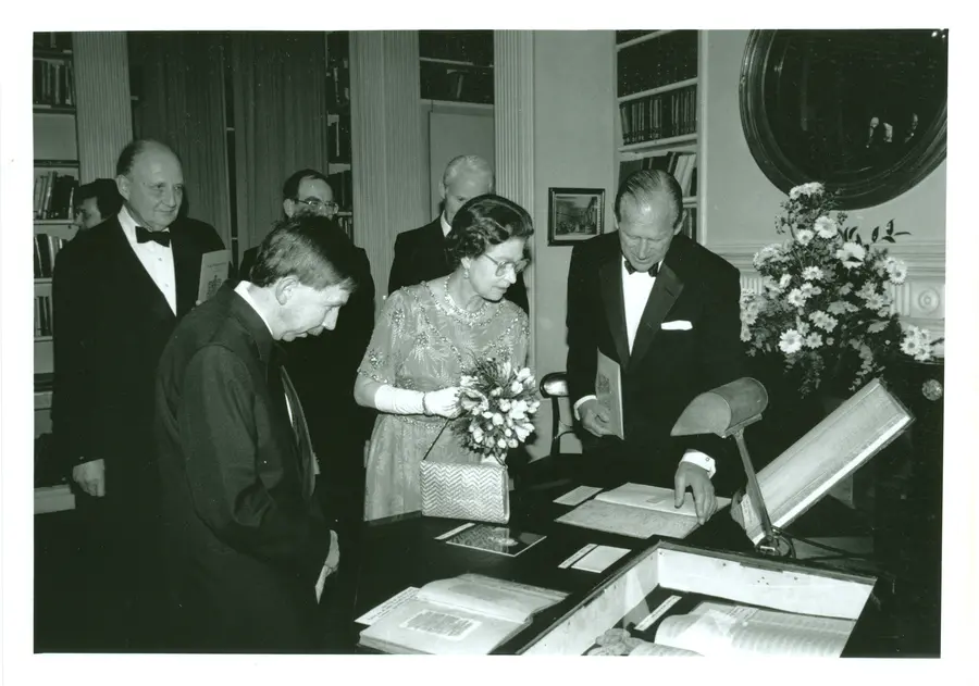 Black and white photograph of Queen Elizabeth holding a bouquet and looking at a handwritten book