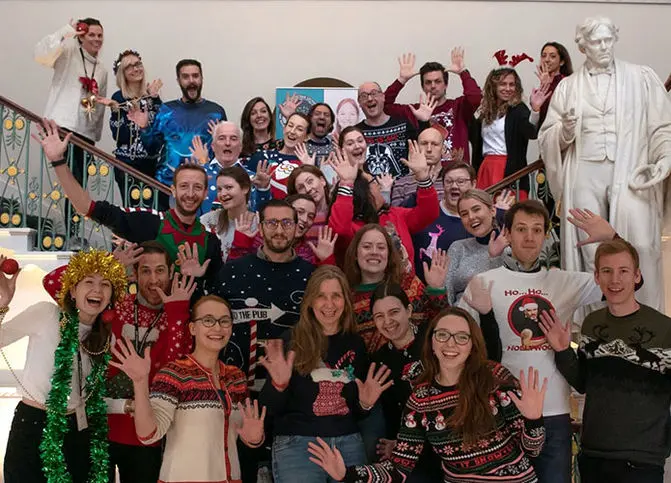 around 30 people in Christmas jumpers waving and smiling at the camera