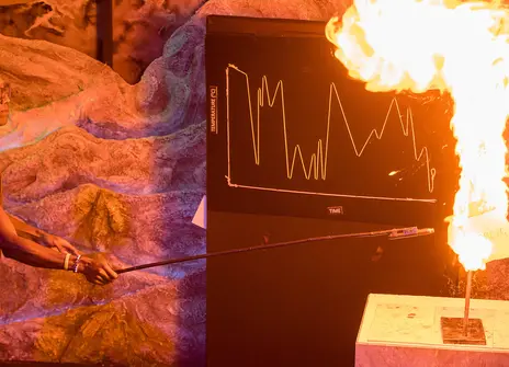 Chris Jackson holding a long stick with a match at the end setting fire to an experiment