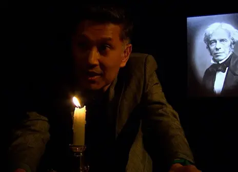 Saiful Islam leaning in front of a lit candle, with a portrait of Michael Faraday in the background