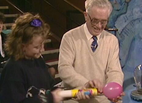 Charles Taylor using a machine to blow up a balloon, with a child in the Ri theatre