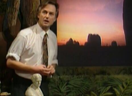 Richard Dawkins speaking next to an photo of a sunset