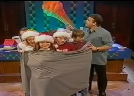 Tony Ryan stands next to a group of children who are standing together, wrapped in a sheet