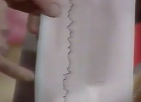 a hand pointing at a piece of paper that has a vertical wobbly line