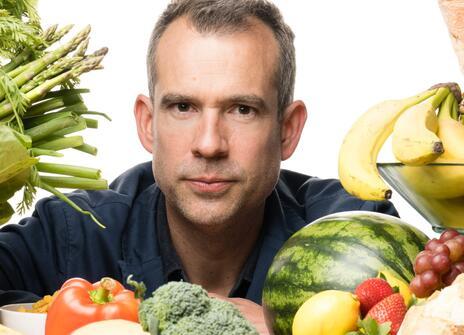 Chris looks into the camera surrounded by different types of food