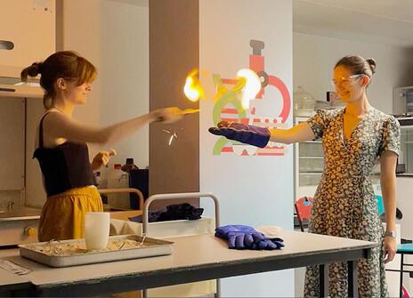 Two women taking part in a science demonstration involving fire, in a lab