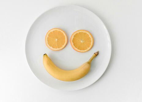 Two orange slices and a banana on a plate, making a smiley face shape