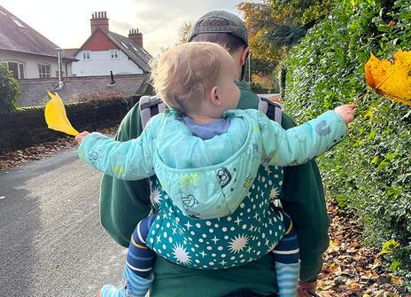 A child with curly blonde hair being carried on an adult's back with a baby backpack