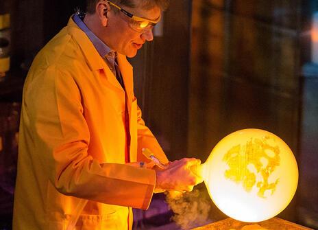 man in yellow lab coat and safety glasses is holding onto a brightly glowing yellow orb