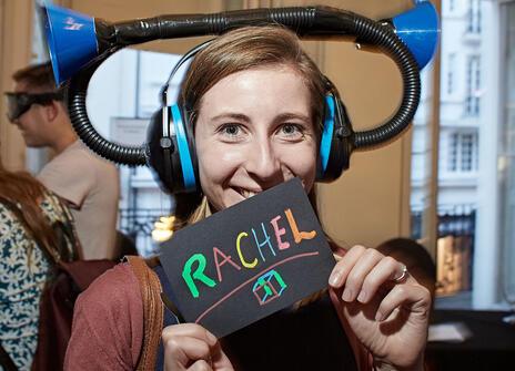 a woman with a trumpet like hat on her head holding a sign that says "Rachel"