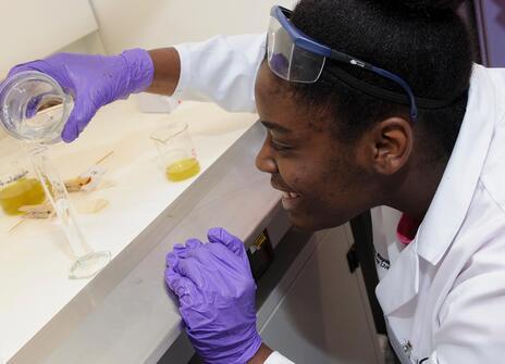 a girl pouring a yellow liquid into a test tube