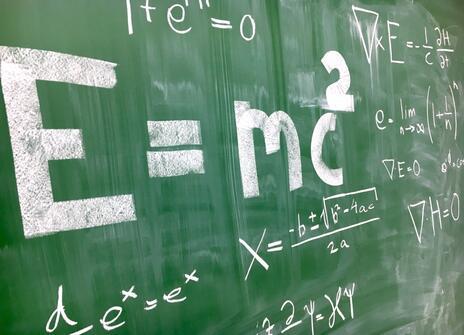 A green chalkboard has the equation 'E=c^2' written in large white letters. 