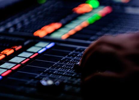 A hand operating a sound mixing machine, with lit up buttons