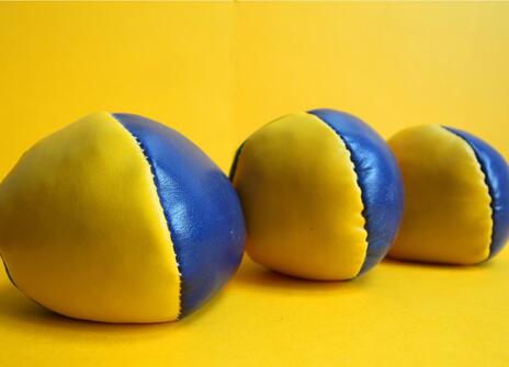 three yellow and blue juggling balls sit on a yellow surface, against a yellow background. 