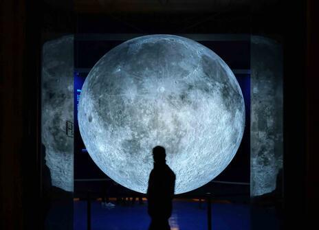 A man walks across a large picture of the moon