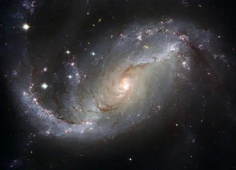 A view of a spiral galaxy, NGC 1672, unveils details in the galaxy’s star-forming clouds and dark bands of interstellar dust.